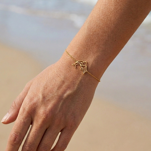 Bracelet doré animal totem dauphin porté à la plage – bijou spirituel femme en acier inoxydable inspiré du dauphin, symbole de liberté, intuition et protection marine.