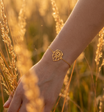 Bracelet animal totem lion en or au design géométrique et minimaliste, porté par une femme dans un champ de blé.