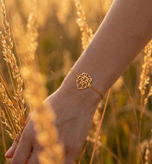 Bracelet animal totem lion en or au design géométrique et minimaliste, porté par une femme dans un champ de blé.