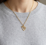 Collier en or pour femme avec un pendentif en forme de loup au style minimaliste et géométrique, porté sur un pull en cachemire gris.