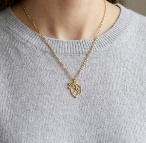 Collier en or pour femme avec un pendentif en forme de loup au style minimaliste et géométrique, porté sur un pull en cachemire gris.