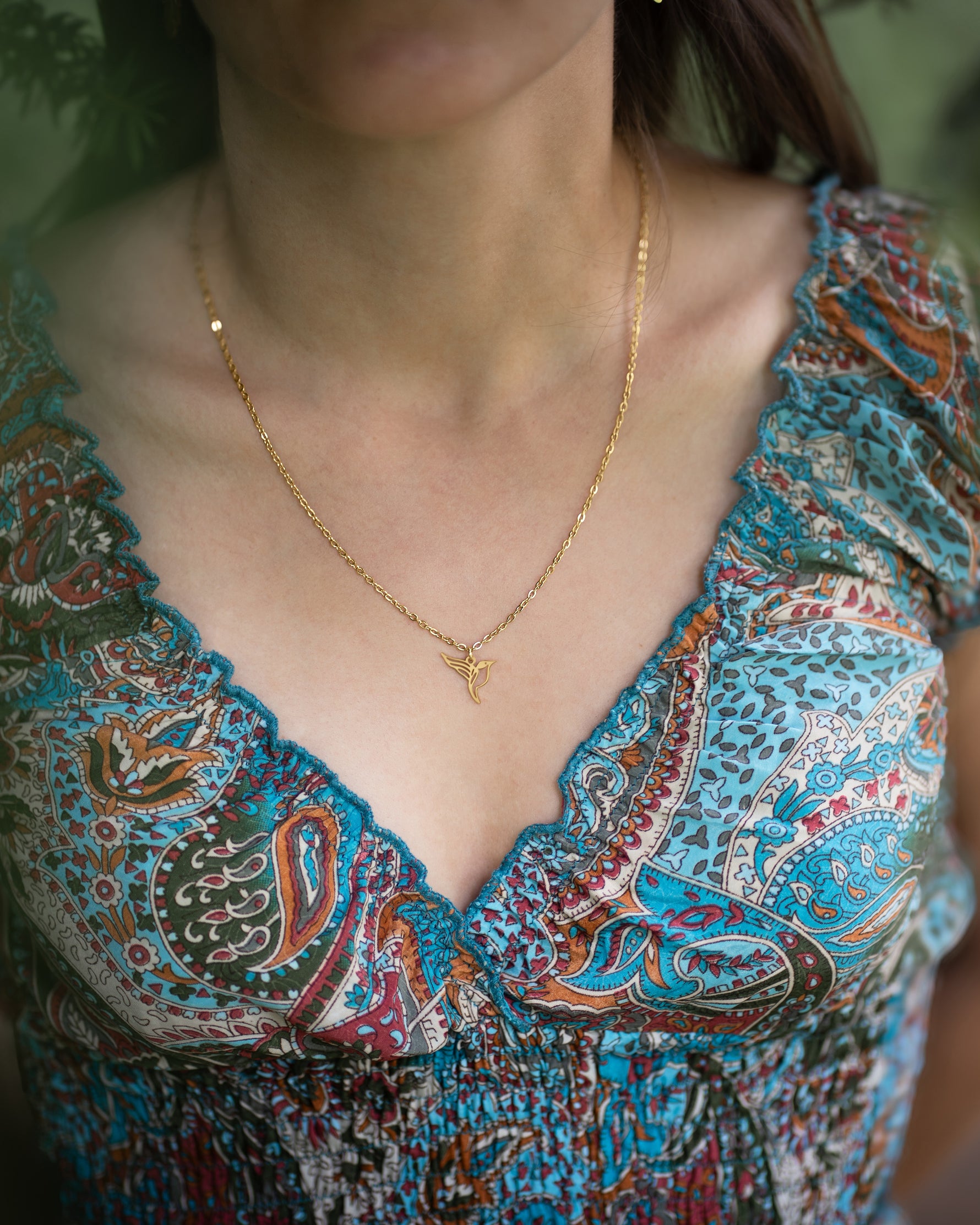 Collier animal totem en acier inoxydable doré avec pendentif colibri style origami géométrique porté par une femme