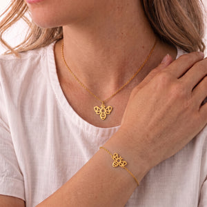Parure de bijoux abeille animal totem LIYAMI Nature : collier et bracelet dorés en acier inoxydable avec pendentifs abeille géométrique, portés par une femme.