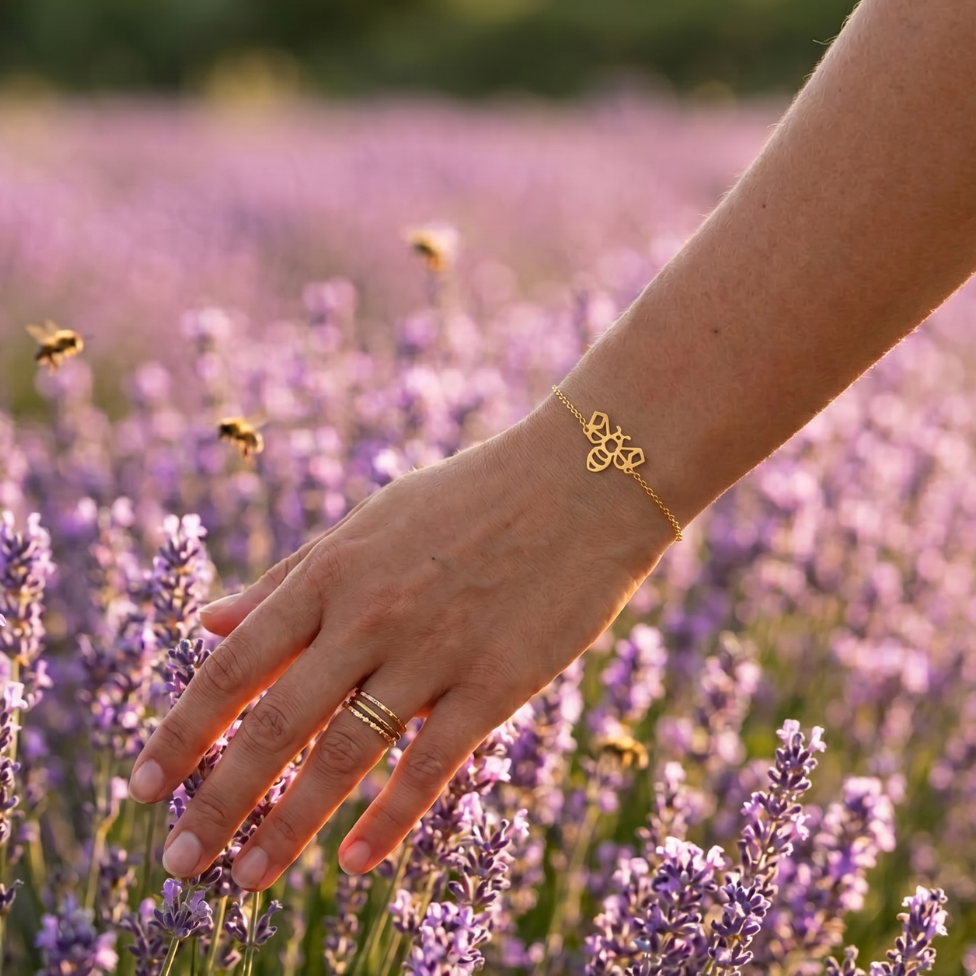 Bracelet abeille doré porté au poignet d'une femme devant un champ de lavande en fleurs, bijou animal totem inspiré de la nature
