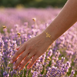 Bracelet abeille doré porté au poignet d'une femme devant un champ de lavande en fleurs, bijou animal totem inspiré de la nature